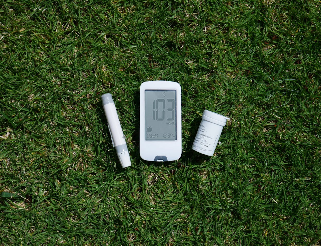 Diabetes management tools including glucose meter and test strips on grass, highlighting outdoor use.